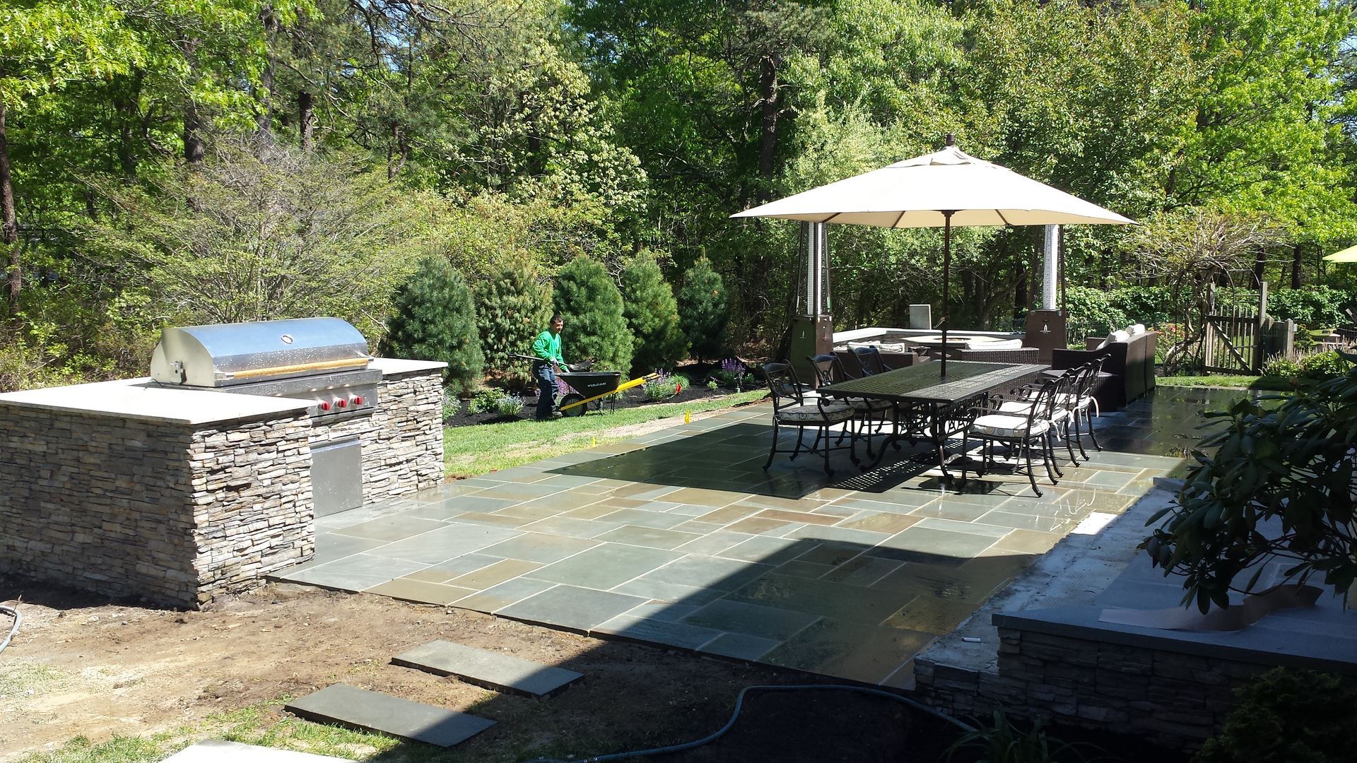A large patio with a table , chairs , umbrellas and a grill.