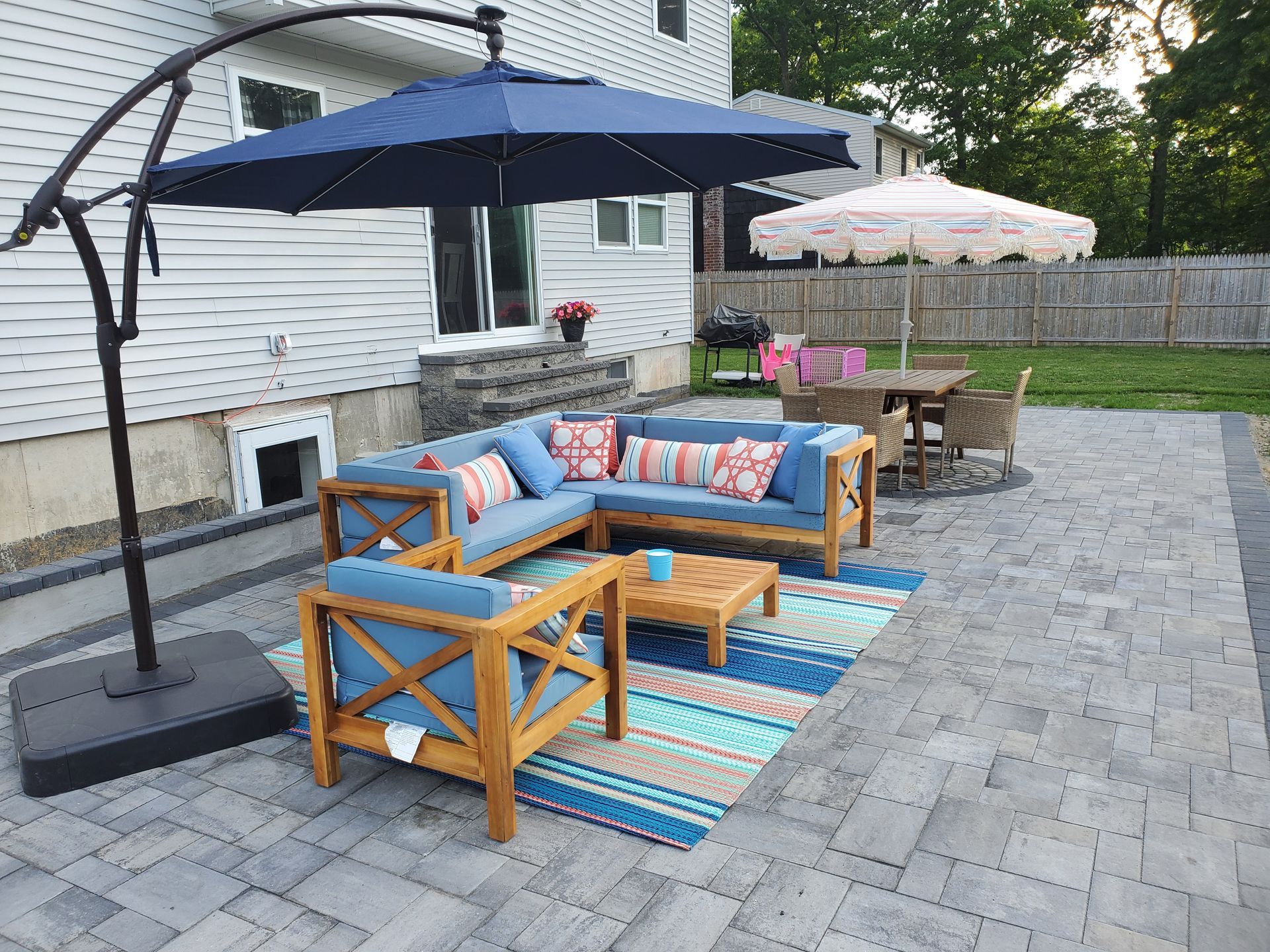 A patio with a couch , chairs , umbrellas and a rug.