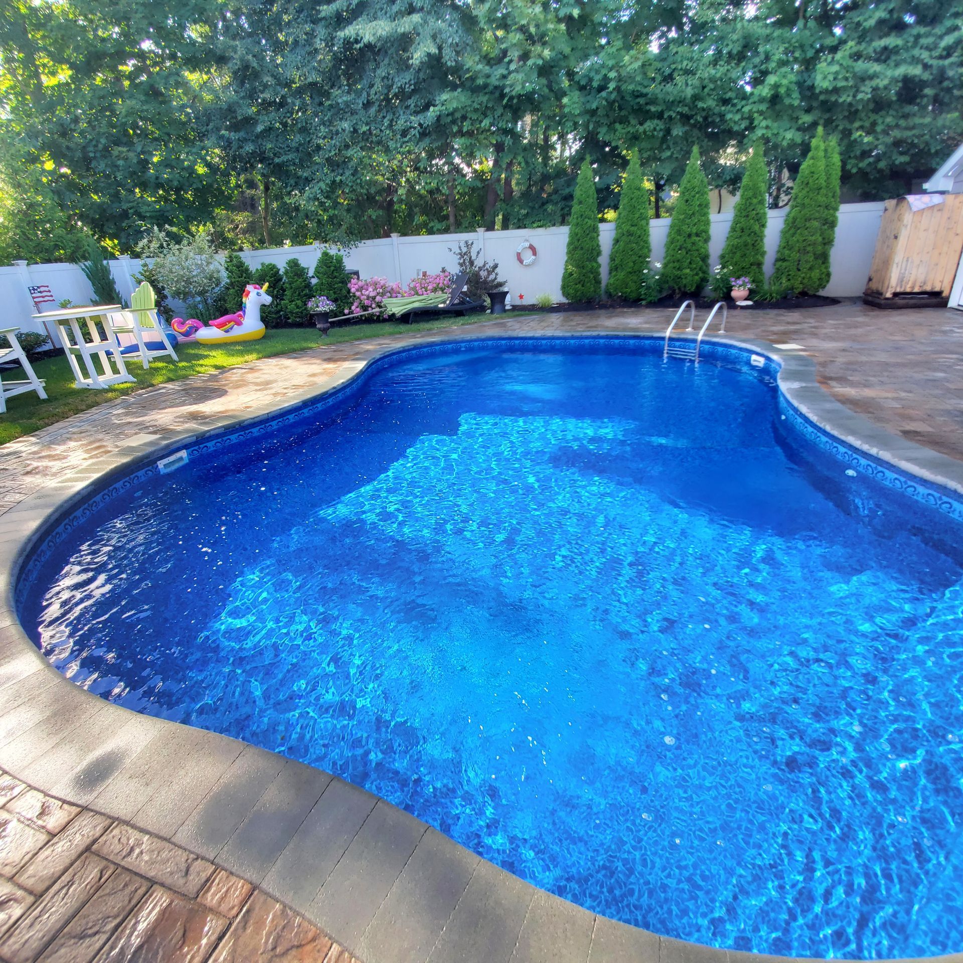 A large blue swimming pool surrounded by trees and chairs