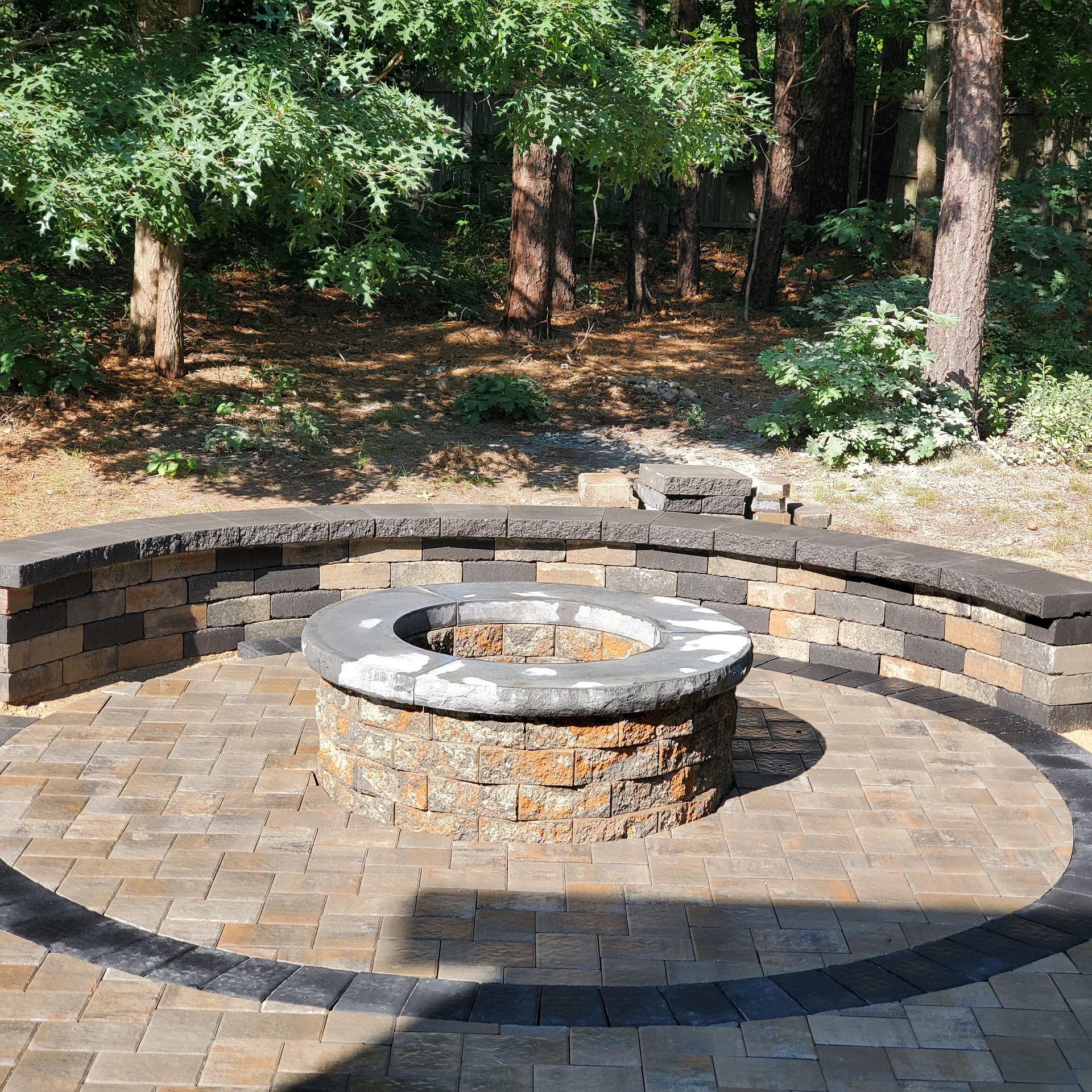 A fire pit in the middle of a brick patio in the woods