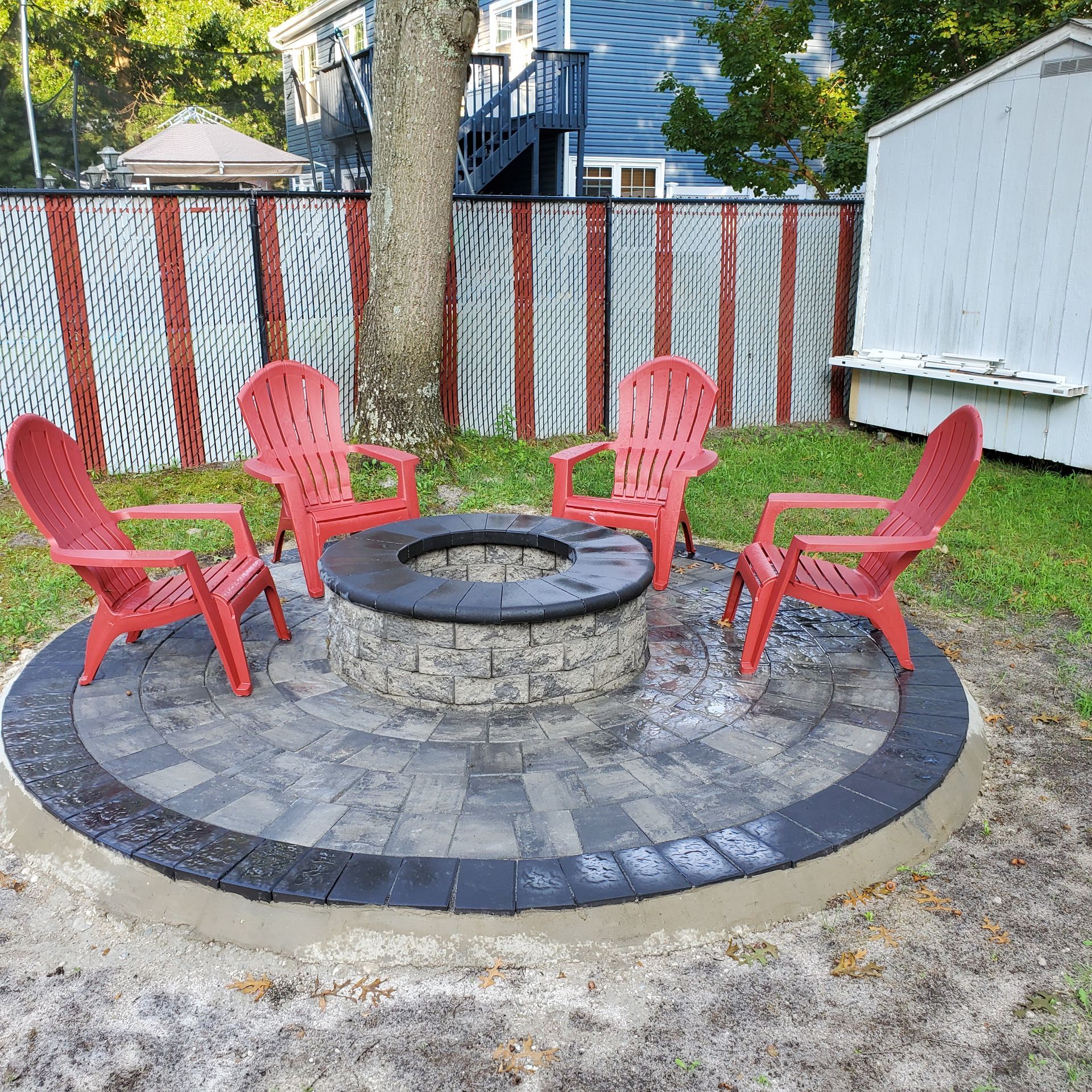 A fire pit with red chairs around it in a backyard.