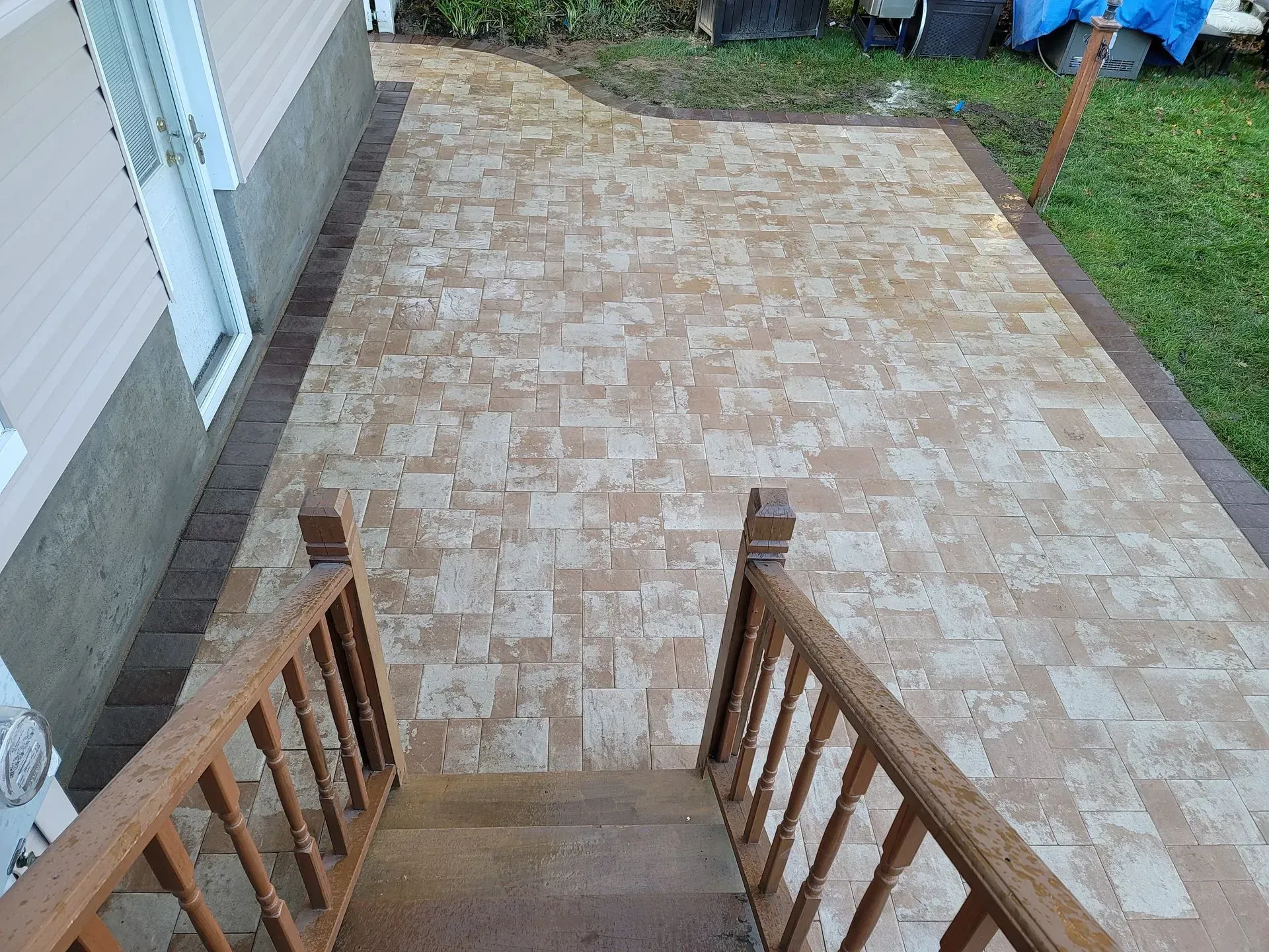 Wooden stairs lead down to a brick patio. The patio is edged with brown brick and has a tan
and brow