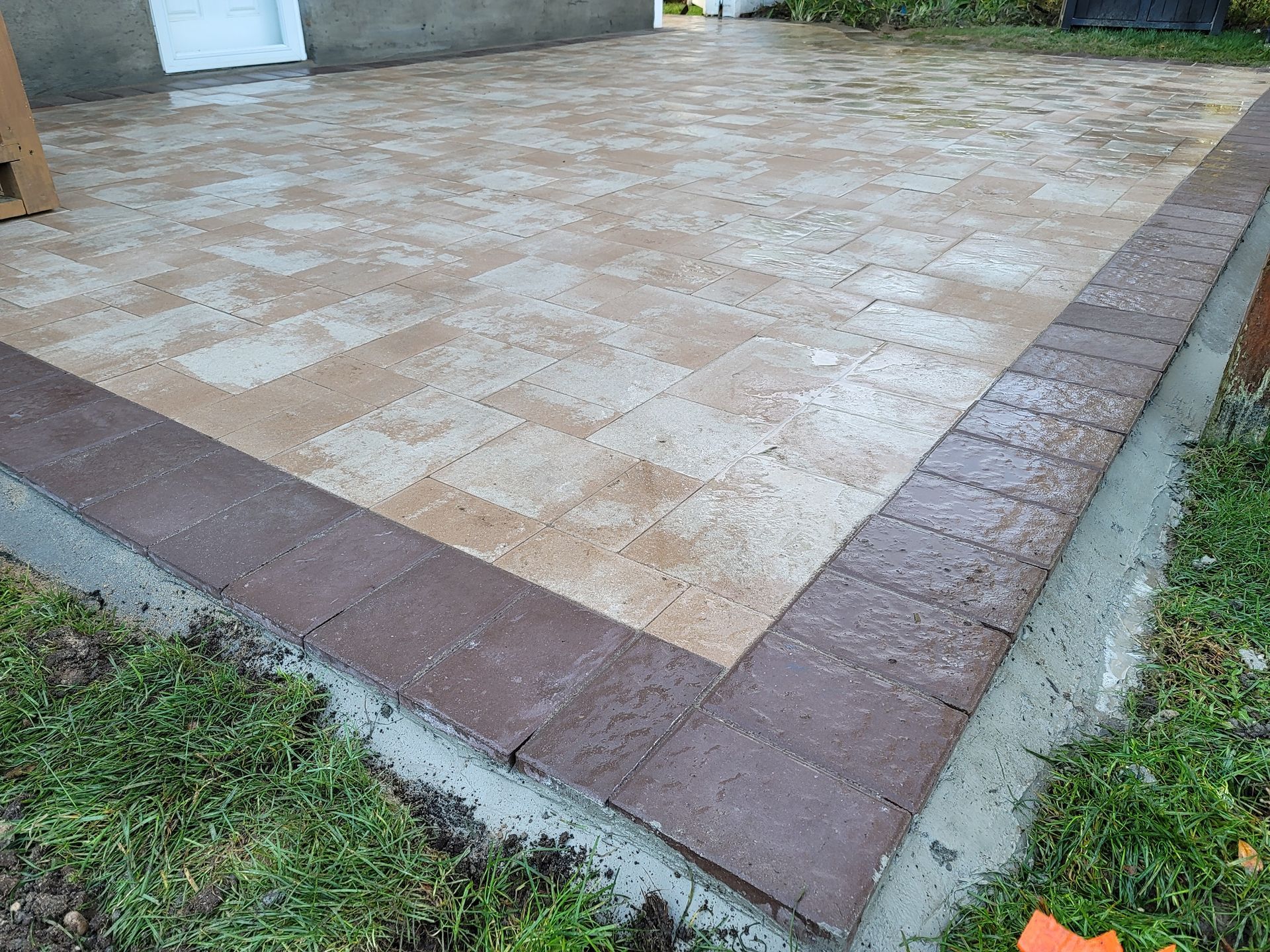 A brick patio with a brown border is sitting in the grass.