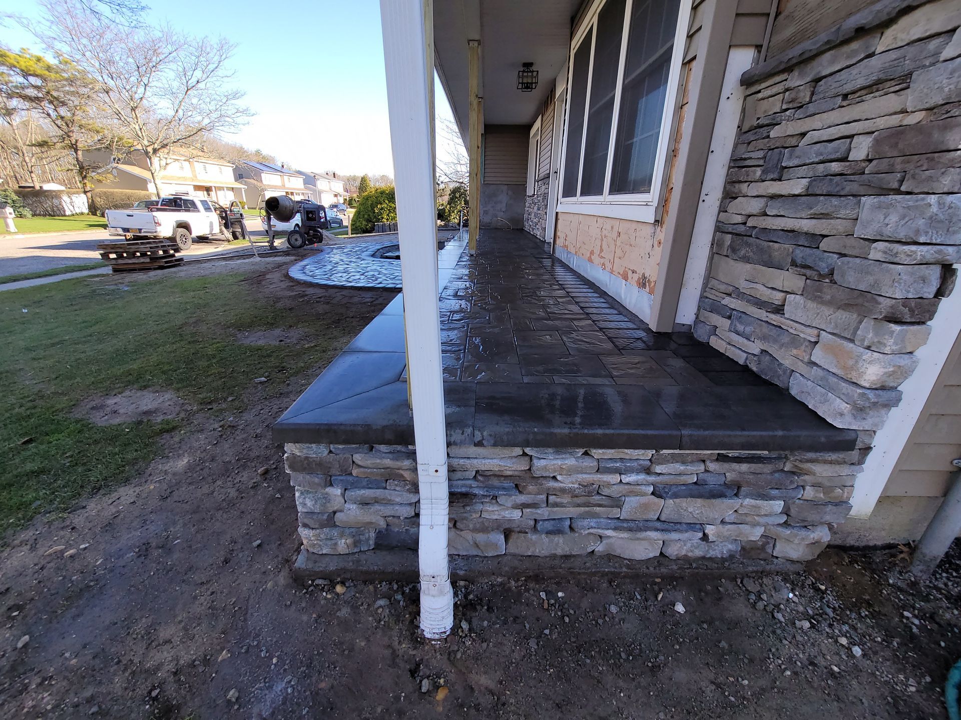 The front porch of a house with a stone wall and a concrete step.
