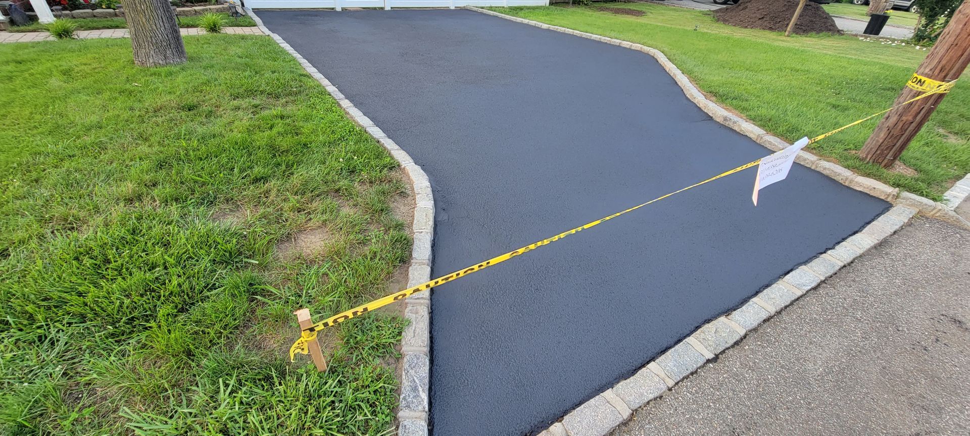 A black driveway with a yellow tape along the side of it.