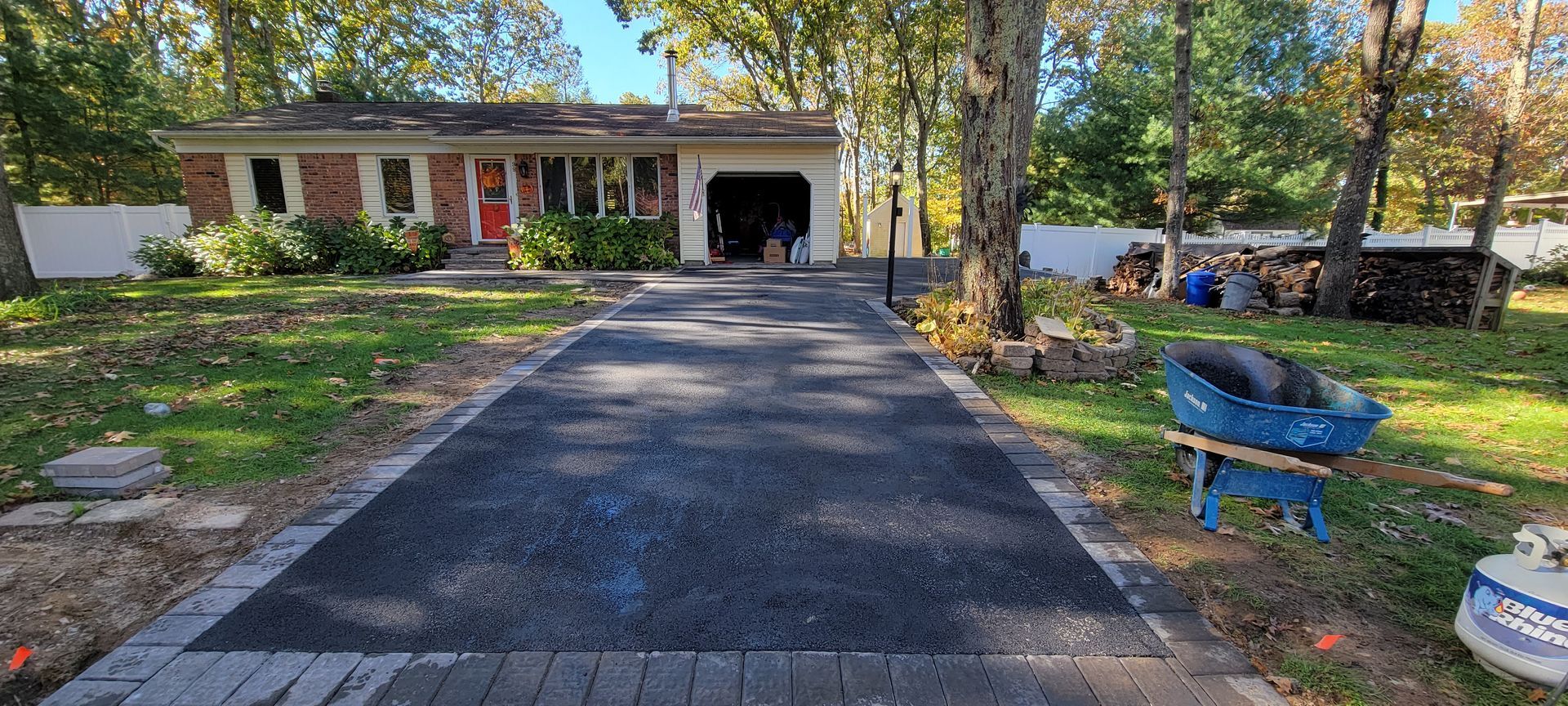 A wheelbarrow is sitting on the side of a driveway in front of a house.