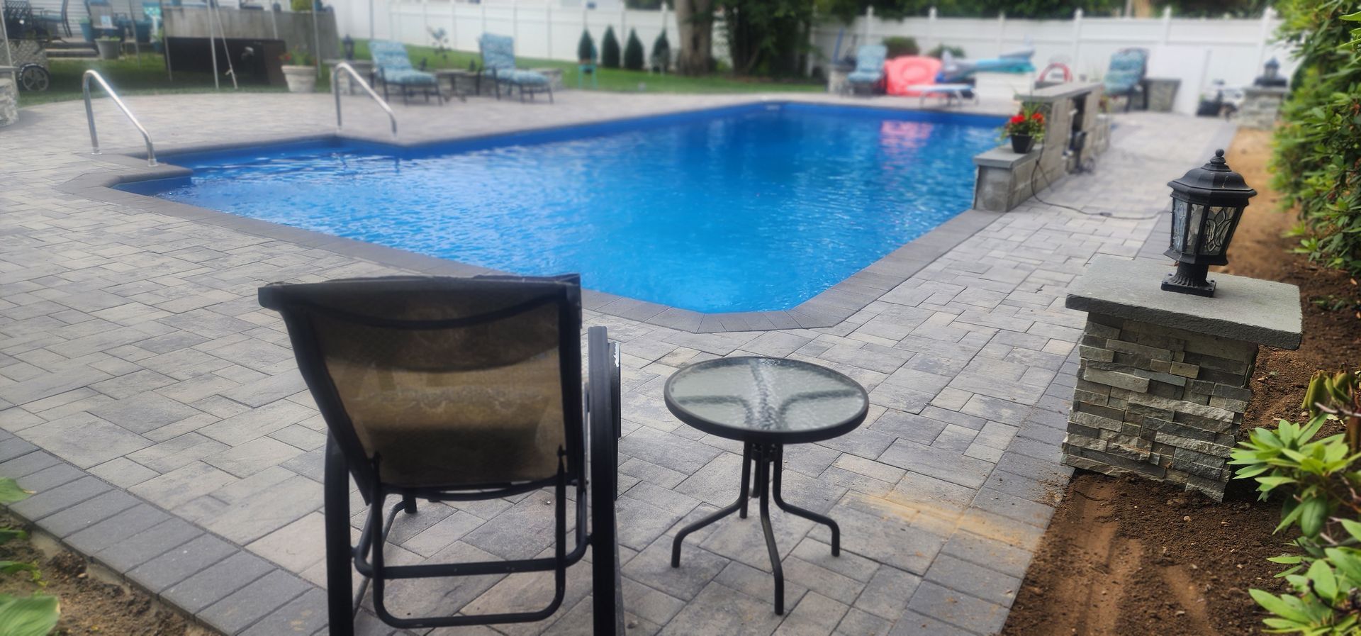 A chair and a table are sitting in front of a large swimming pool.