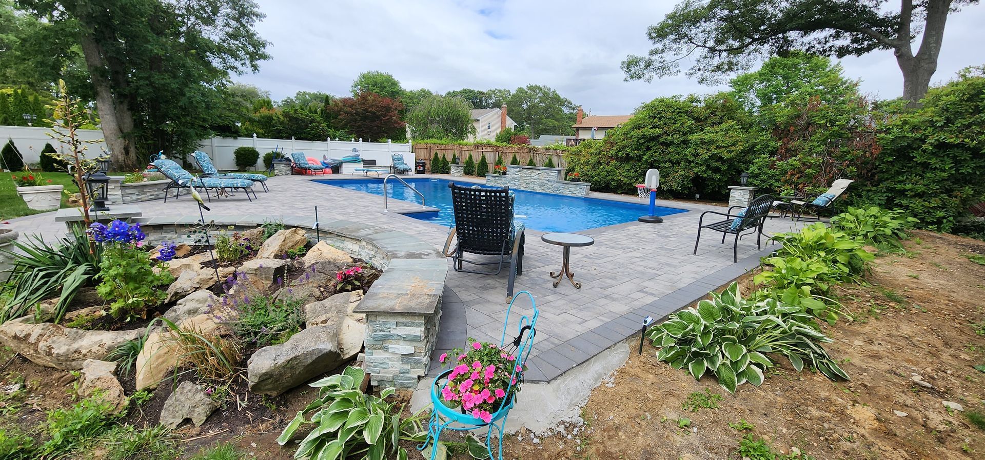 A large swimming pool surrounded by rocks and flowers in a backyard.