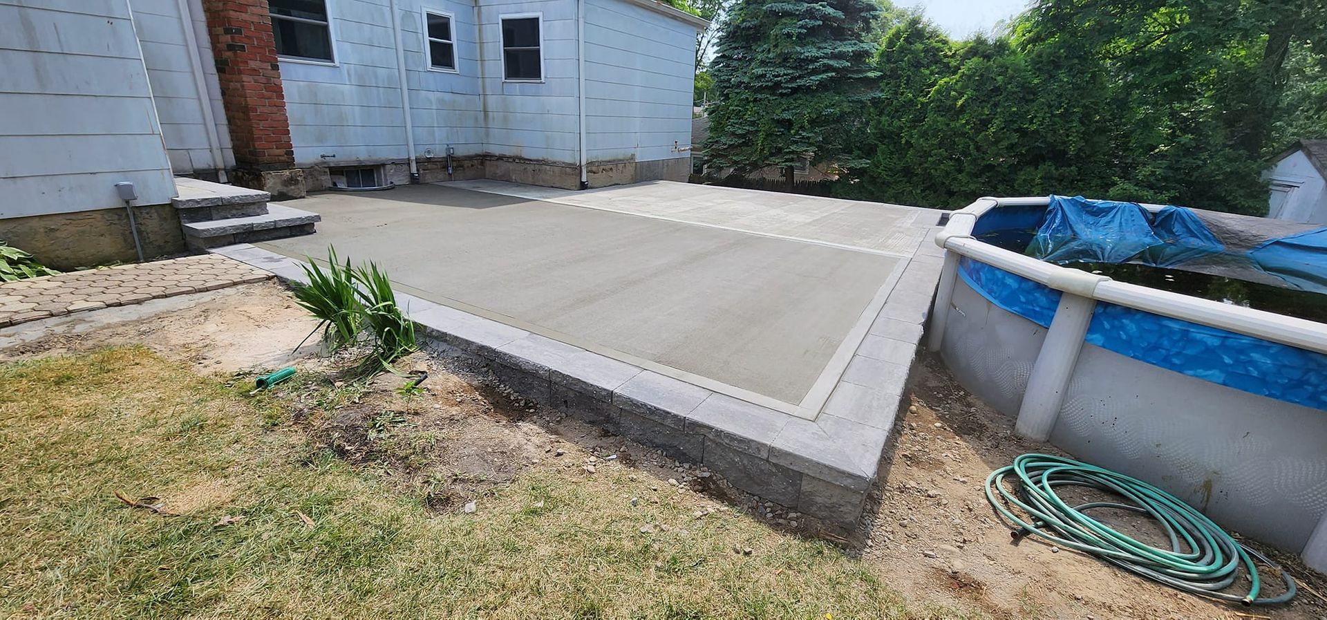 A concrete patio is being built next to a pool in a backyard.