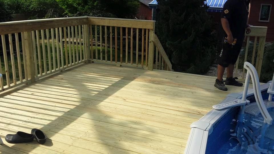 A man is standing on a wooden deck overlooking a swimming pool.