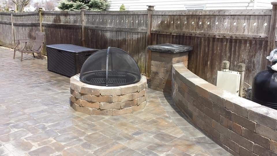 A fire pit is sitting on a brick patio next to a wooden fence.