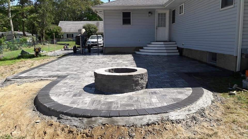 A fire pit is in the middle of a patio in front of a house.