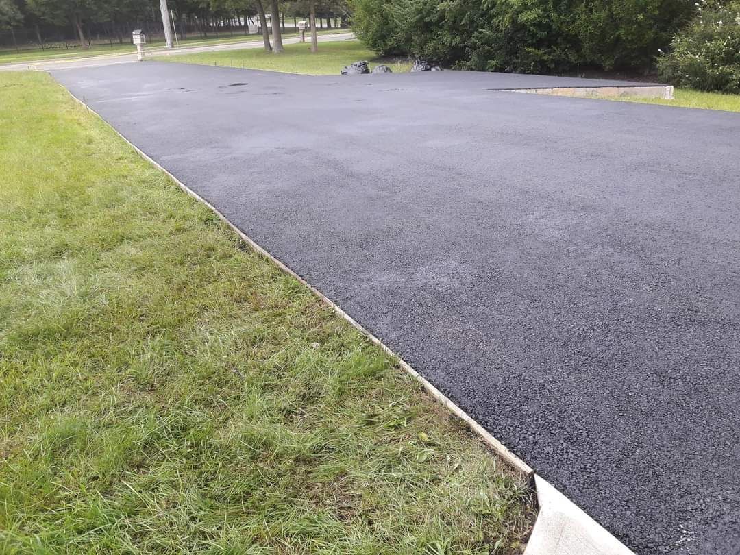A black asphalt driveway surrounded by grass and trees.