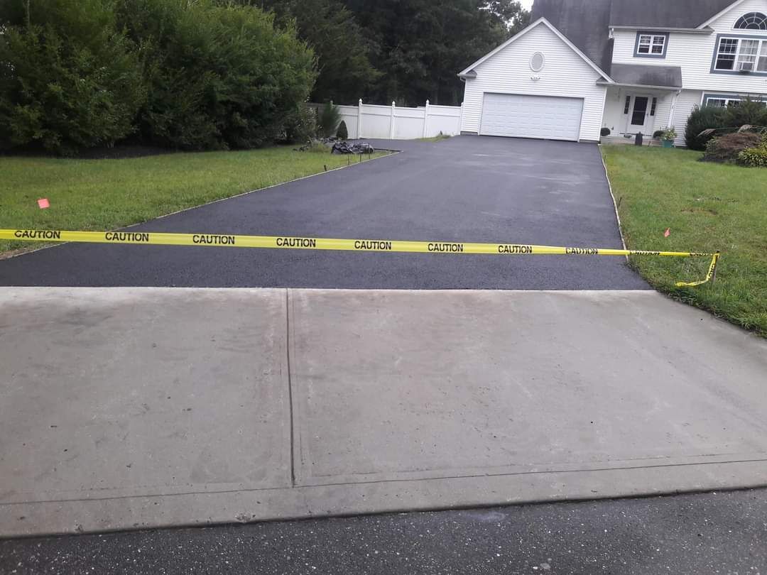 A driveway with a yellow tape covering it and a house in the background.