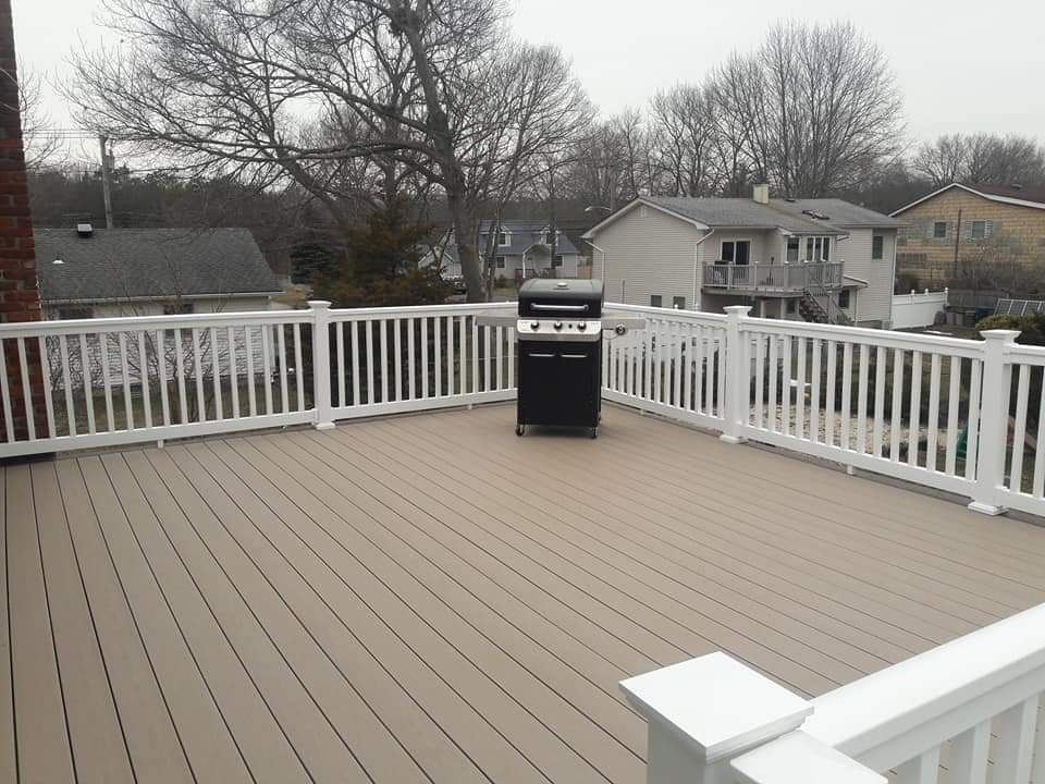 A deck with a grill on it and a white railing
