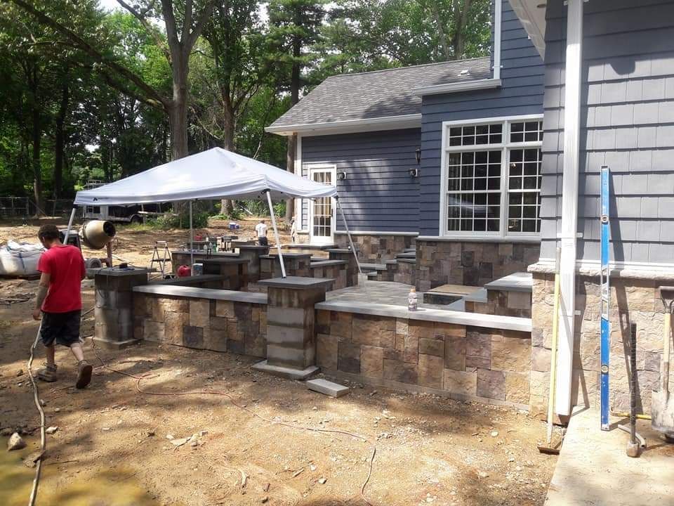 A man in a red shirt is walking in front of a house under an umbrella.