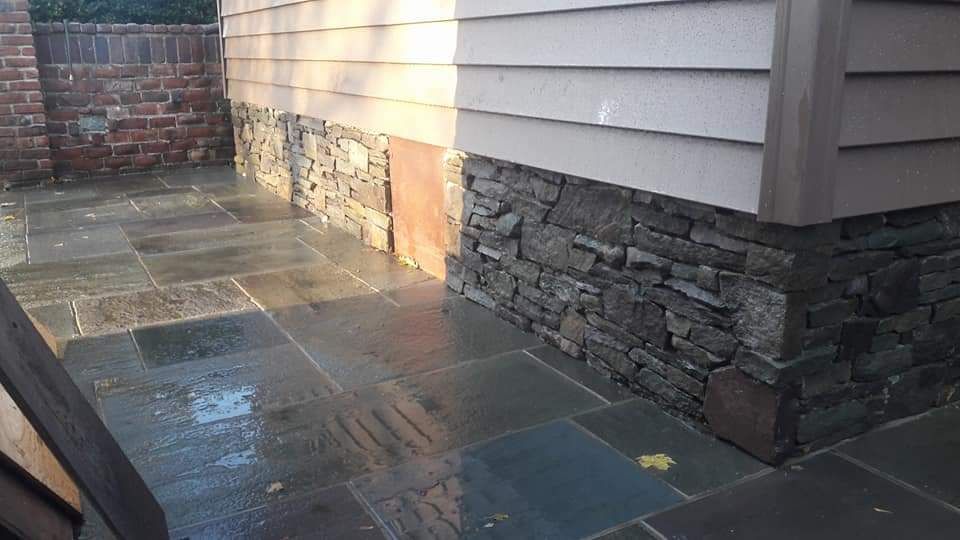 A stone walkway next to a house with a brick wall.