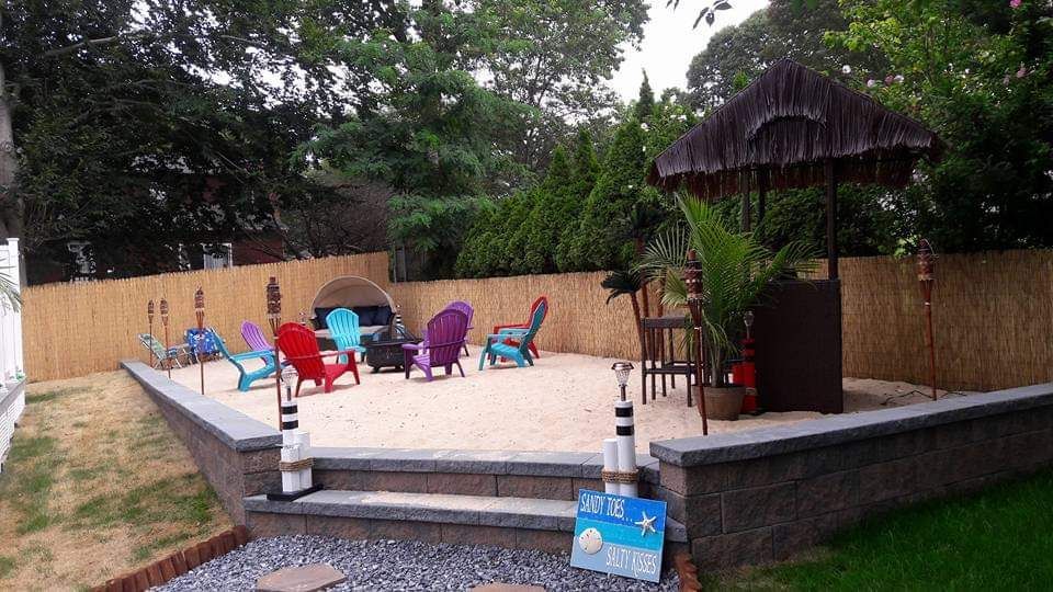 A backyard with a sandy area with chairs and umbrellas.