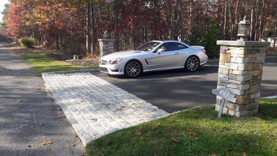 A silver sports car is parked in a driveway next to a stone pillar.