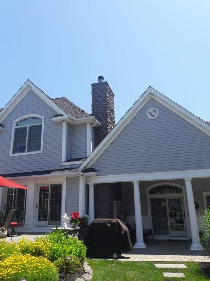 A large gray house with a porch and a grill in the backyard.