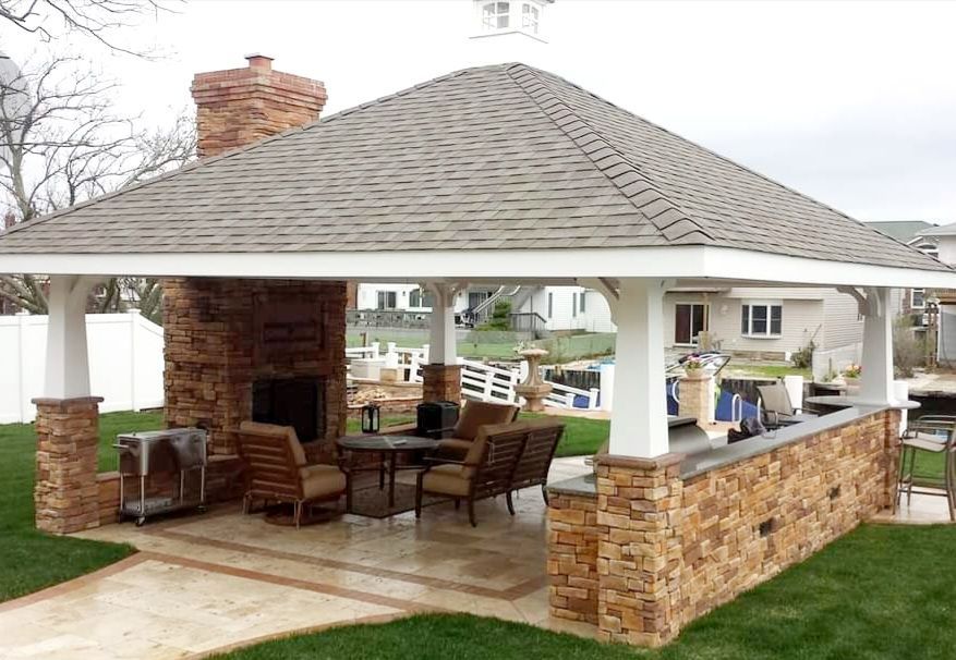 A gazebo with a fireplace and tables and chairs in a backyard.