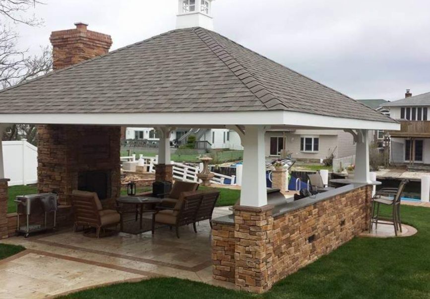A gazebo with a roof and a fireplace in the backyard of a house.