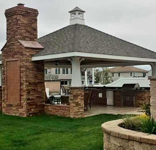 A gazebo with a chimney and a grill in the backyard of a house.