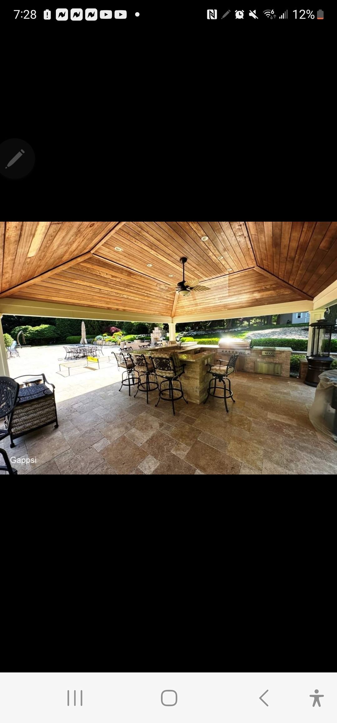 A picture of a patio with tables and chairs under a wooden roof.