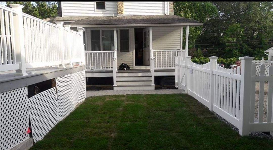 A white fence surrounds a lush green yard in front of a house.