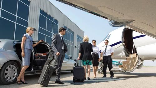 People exiting a limousine and boarding a private jet on a sunny tarmac; pilot assists with luggage.