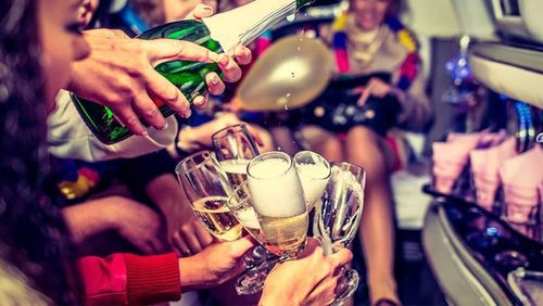 People in a vehicle celebrating with champagne, pouring into glasses, with blurred background of other partygoers.