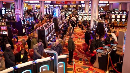 Casino floor with many slot machines, people playing, and colorful carpeting.