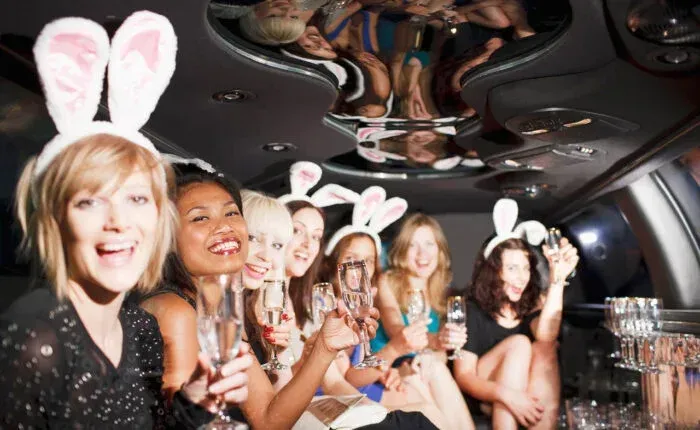 Women in bunny ears celebrate with champagne inside a limo, looking happy and excited.