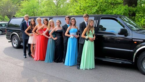 Group of teens in formal wear poses by a black limousine on a sunny day.