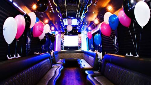 Inside of a party bus with balloons in pink, blue, black, and white. Blue and purple lights line the walls.