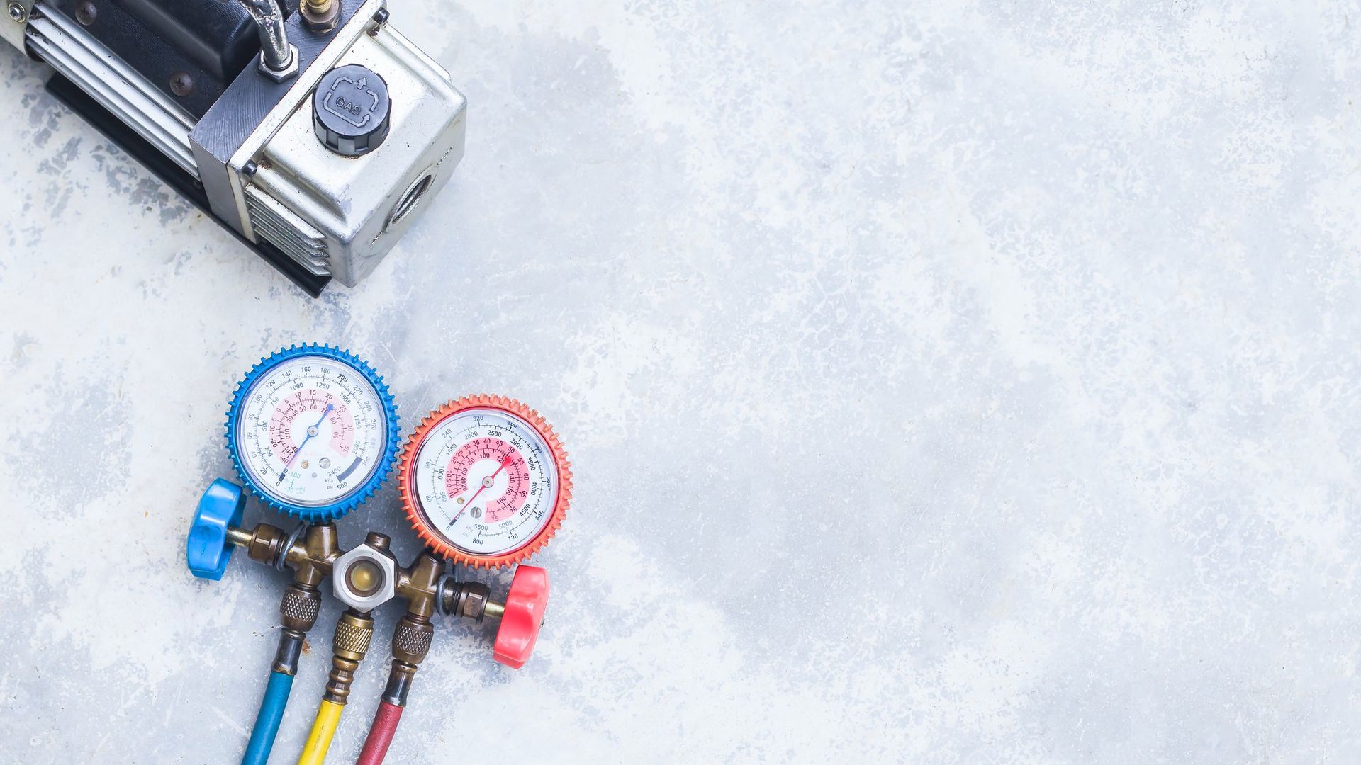 HVAC technician inspecting gauges. Blue and red pressure gauges in hand, wearing gloves and a blue plaid shirt.
