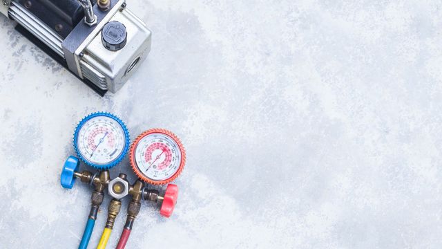 HVAC technician inspecting gauges. Blue and red pressure gauges in hand, wearing gloves and a blue plaid shirt.