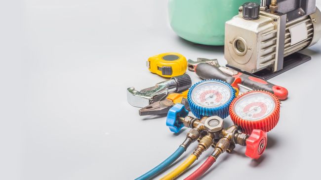 Smiling worker in overalls standing near installed air conditioner units.