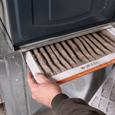A hand removing a dirty air filter from an HVAC unit.