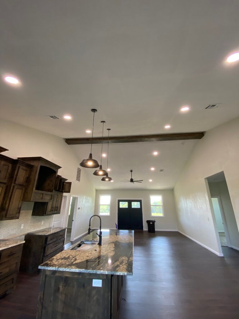 An open-concept kitchen and living area with dark wood cabinets, a granite island, pendant lights, and a wooden ceiling beam.