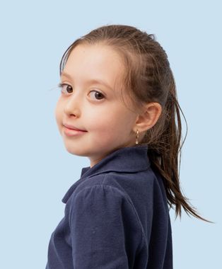 A young boy wearing a blue shirt is smiling in front of an orange background