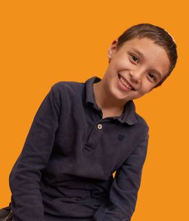 A little girl wearing a blue shirt and earrings looks at the camera