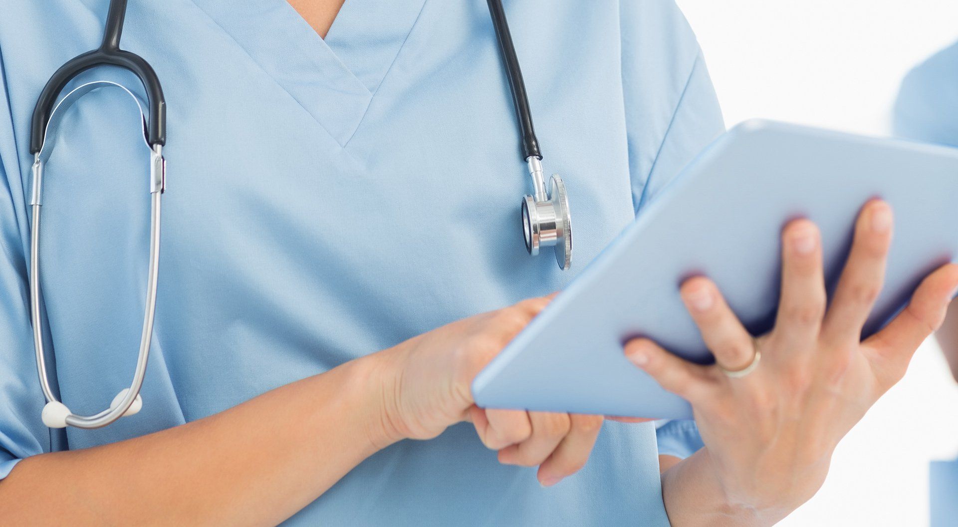 Nurse in blue scrubs, stethoscope, using tablet.