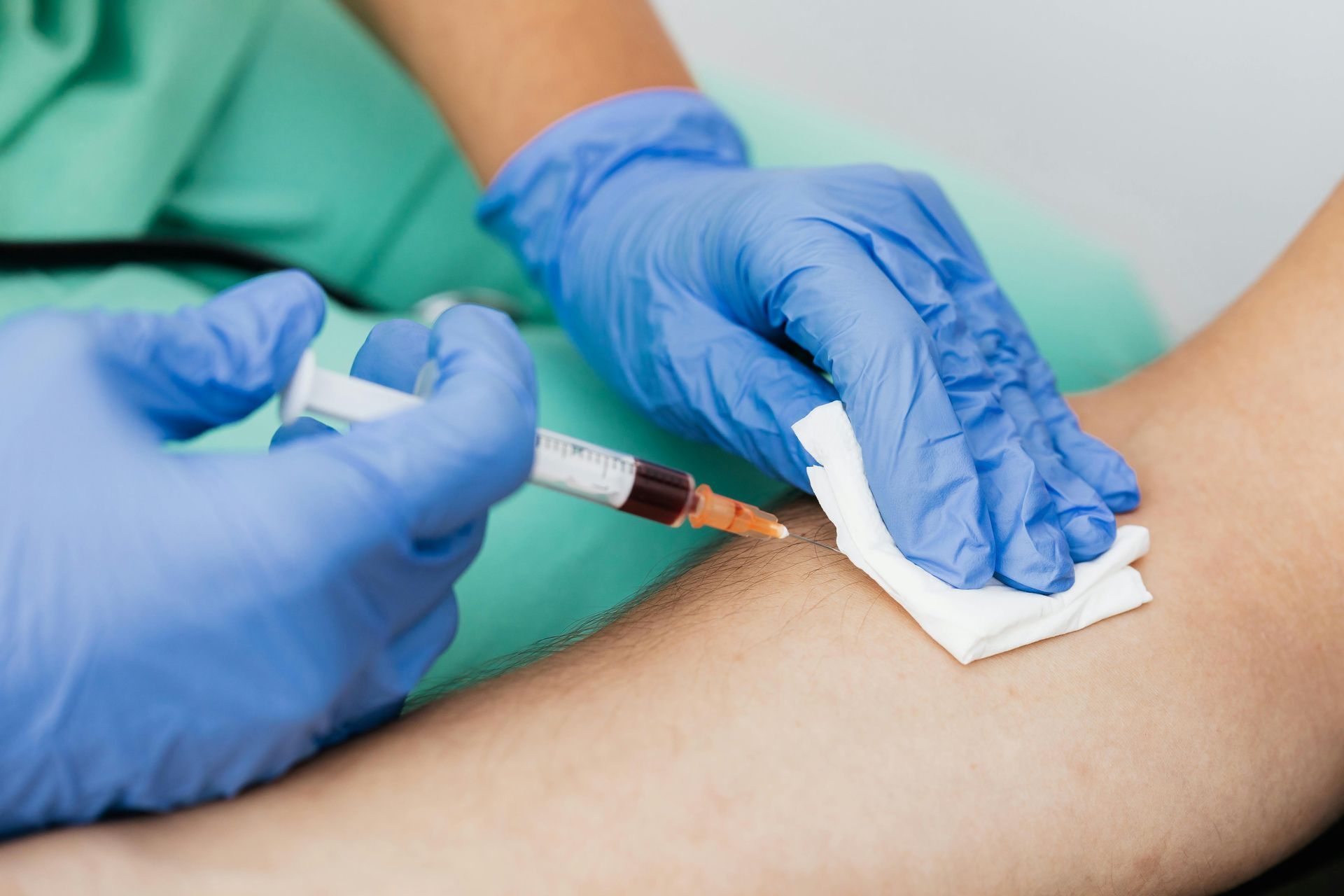 Person in blue gloves drawing blood from a patient's arm with a syringe, in a medical setting.