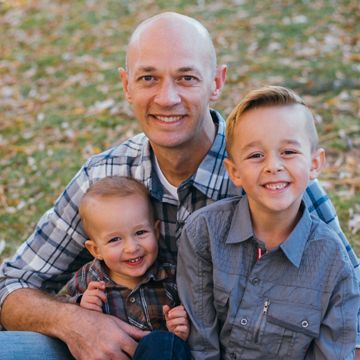 Man with two young sons smiling outdoors, fall setting.