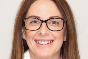 Woman with brown hair and glasses smiling directly at the camera.