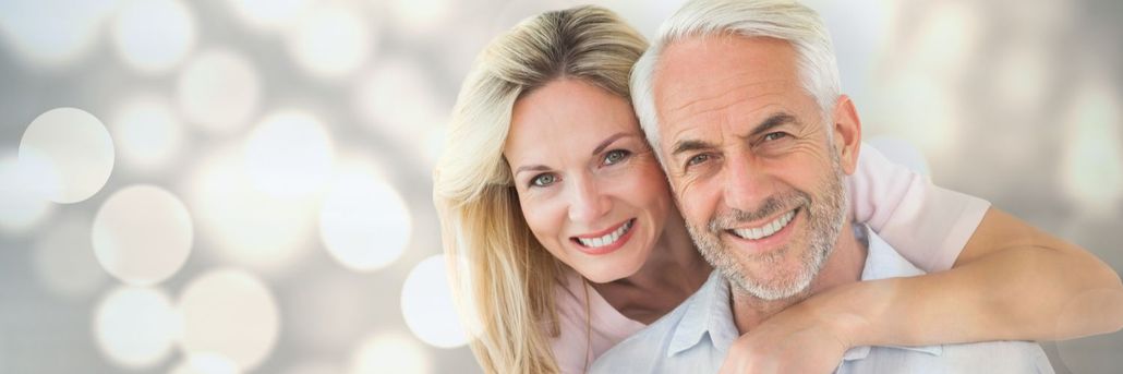 Smiling couple, the woman with blonde hair hugging the man from behind, bokeh background.