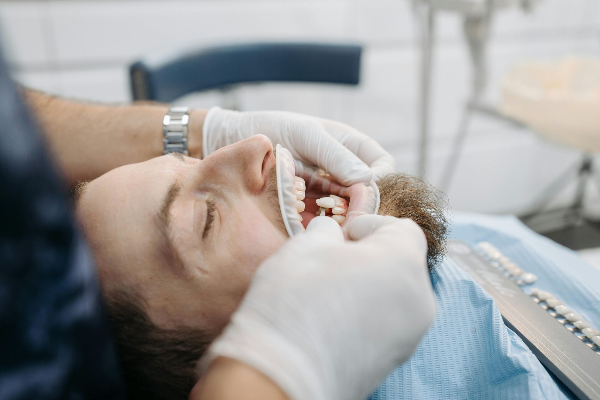 A dentist working on a patient's teeth. The patient lies back with their mouth open, a cheek retractor in place.