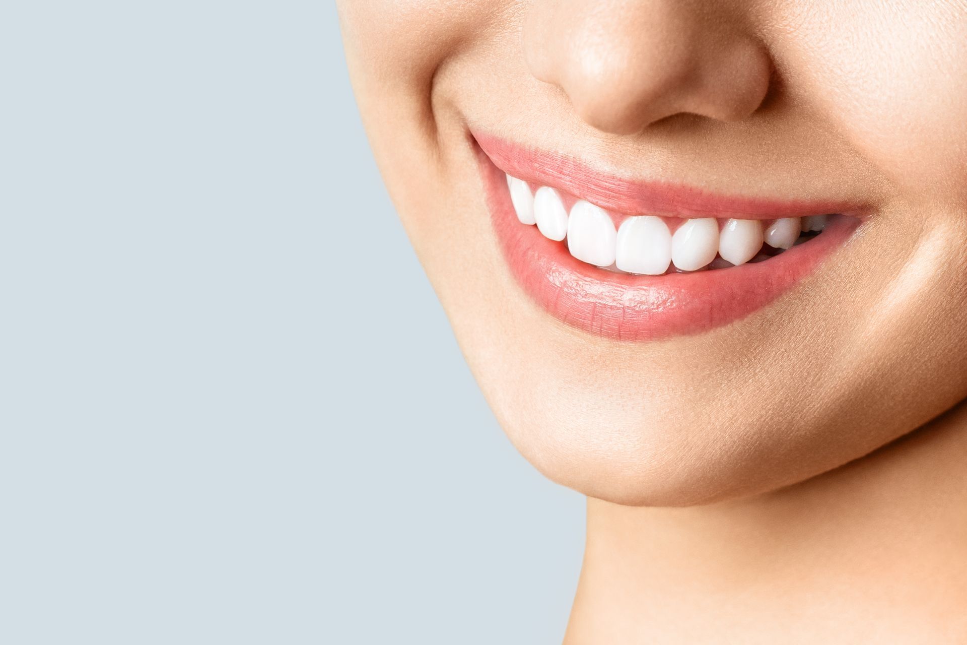 Close-up of a person's smiling mouth, showing bright white teeth and pink lips.