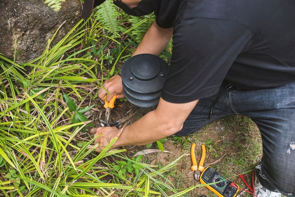 Person Kneeling, Using Wire Cutters on Cable Near Outdoor Light Fixture — CDT Electrical in Byron Bay, NSW